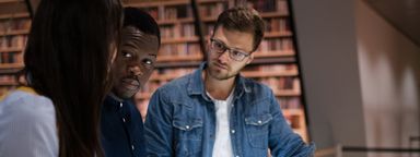 Three people in a library discuss an exhibition