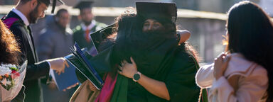 Graduate hugging loved one outside 