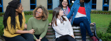 A group of female-presenting students sit on a bench outside Regent Court