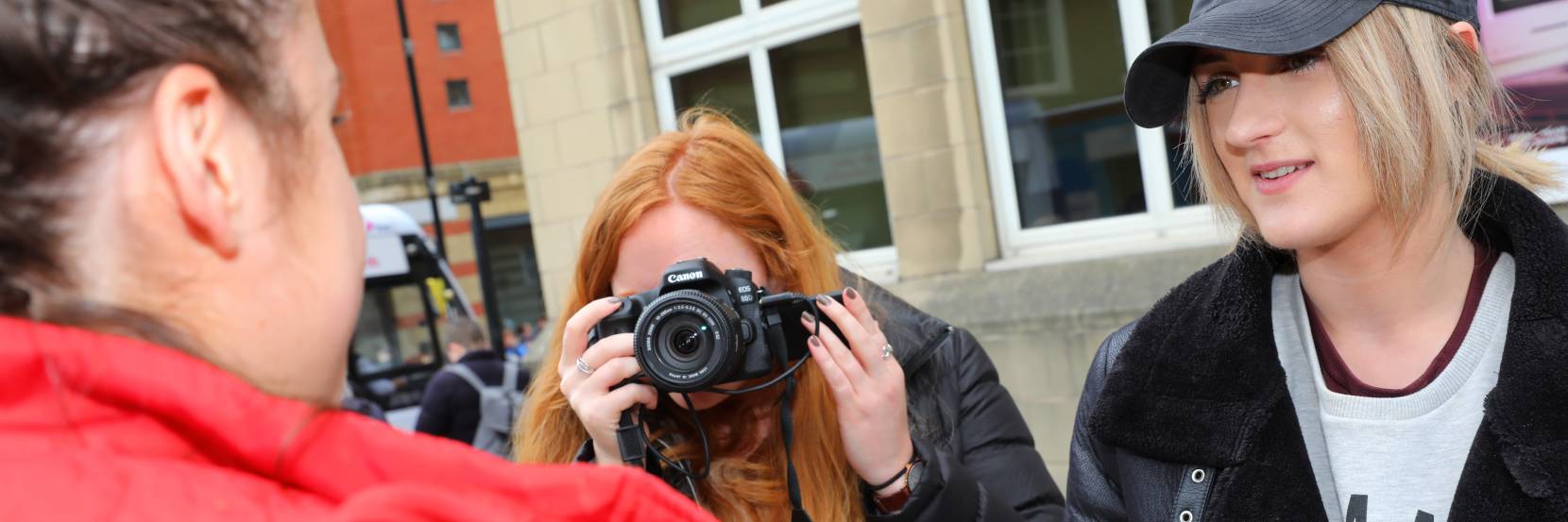 Two journalism students interviewing a member of the public, using a camera and mic