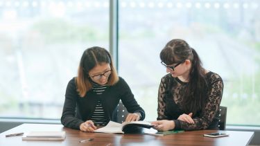 Two postgraduate students studying at a table 