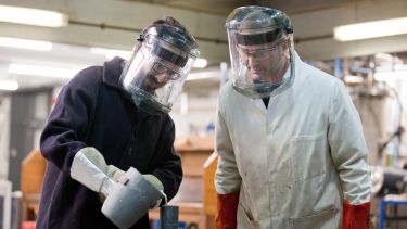An image of student and supervisor in protective clothing in a materials engineering lab