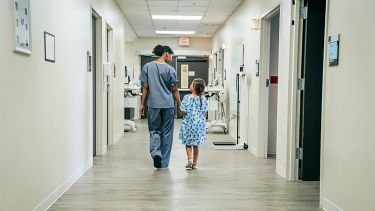 A photograph of a nurse walking with a child down a hospital corridor.