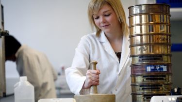 A person in a lab coat using a pestle and mortar