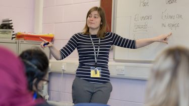 A PGCE student is at the front of a classroom, asking their pupils questions about the work on a white board - image