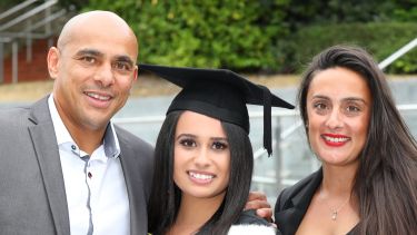 A graduate with her mum and dad. They are smiling. 
