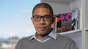 Dr Antony Williams sits infront of a bookshelf and window - image