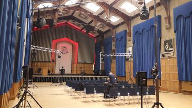 An empty university concert hall rigged up with a stage, sound equipment and lights.