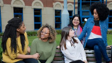 Five female students chat on a bench in the courtyard of the School of Health and Related Research.