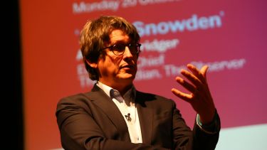 Former Guardian newspaper editor Alan Rusbridger giving a talk. He is in front of a presentation.