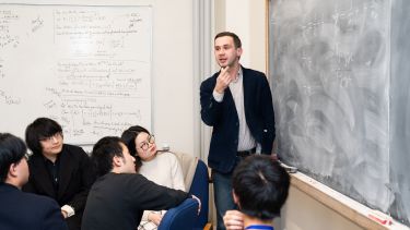 A tutor stood by a chalk board talking to students