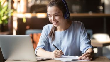 Adult learner at her laptop while writing in a notebook