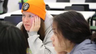 Two girls, one in an orange hat, sit at a desk