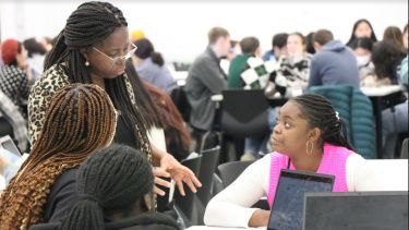 Bina Ogbebor speaks to three students sat at a table.