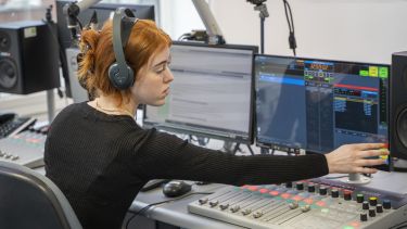 A girl wearing headphones sat at an audio mixing desk 