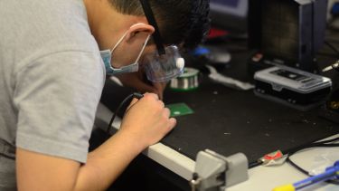 Photograph of Aiman working on soldering in the lab