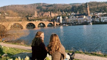Two girls viewed on the back sitting by a river in Germany