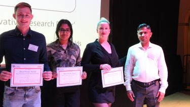 Four people on stage, three holding up prize certificates