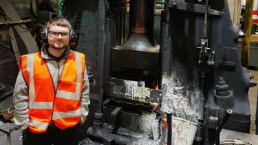 Sam Lister stands next to an industrial hammer at W. H. Tildesley