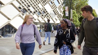 Three students walking in the sun outside of the Diamond building