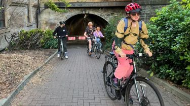 The author of the text on a bicycle with a red helmet just emerging from a tunnel, with some more cyclists in the backround
