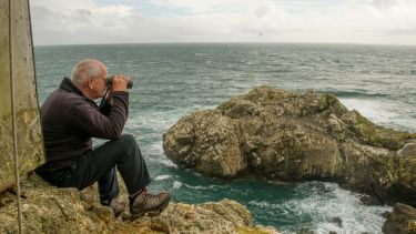 Professor Tim Birkhead sat on a cliff edge watching seabirds