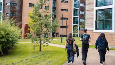 Three students walking away from the camera with accommodation buildings in the background