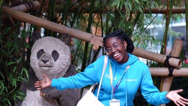 A black girl in a light blue hoodie posing next to a statue of a panda