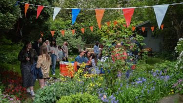 view of a garden with orange bunting and spring flowers. Students standing around in groups talking and laughing