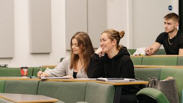 Two students sit next to each other in a lecture hall