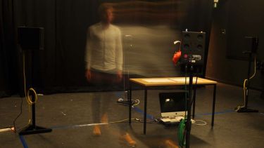 A ghost-like figure surrounded by a table and audio equipment