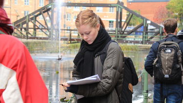 A student sketches in front of a river bridge