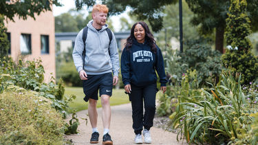 A male and female student walking towards through endcliffe with lots of greenery around them