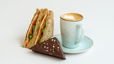 A cheese salad sandwich with a mug of coffee and a triangular brownie 