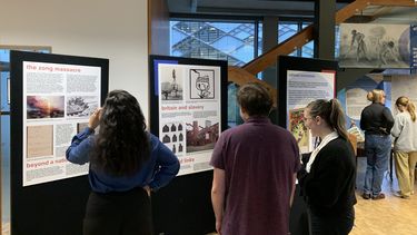 three people seen from the back are looking at exhibition panels. On the first it says The zong massace and beyond the national narrative