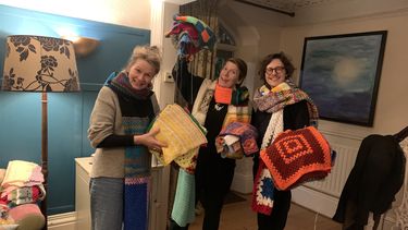 Three people with big scarves on showing off the home knit and crochet squares