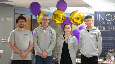 4 members of team standing for photo with Grey Emerge hoodies on with balloons in background