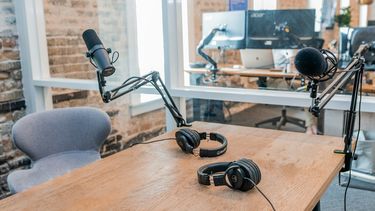 Two microphones and headphones on a table with monitors in the background