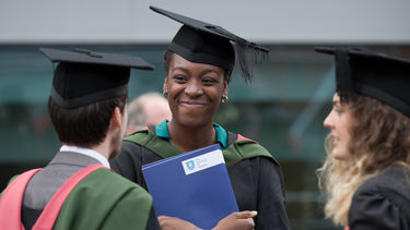 girls smiles in a graduation gown holding her graduation certificate 