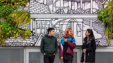 Three students standing next to a brightly decorated building.