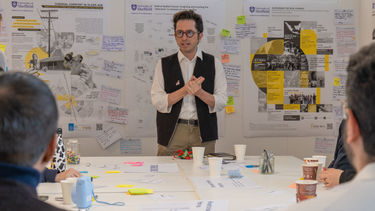 A PhD student presents his poster to a group of people