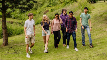 Six students walking along the grass