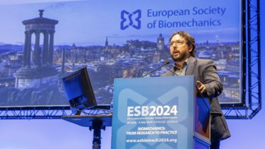 A man wearing glasses stood at a podium for the ESB2024 congress with a background image of the city of Edinburgh.