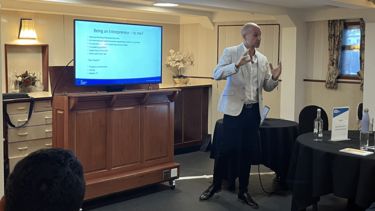 A man delivering a presentation in a ship's meeting room.