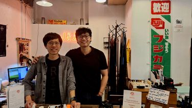 Two men standing behind desk in shop smiling at camera