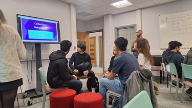 Group of students chatting in a room sat down on chairs