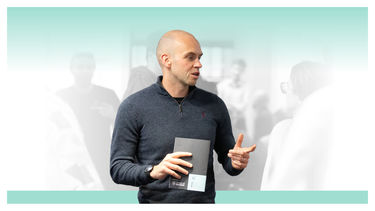 A man in casual dress talking while holding a brochure