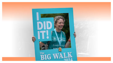 A participant at the finish line of the Big Walk, having their photo taken with a banner