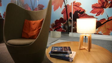 A chair next to a table with books and a lamp