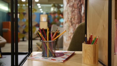 pots of crayons on a bookshelf, with the Garden Room in the background 